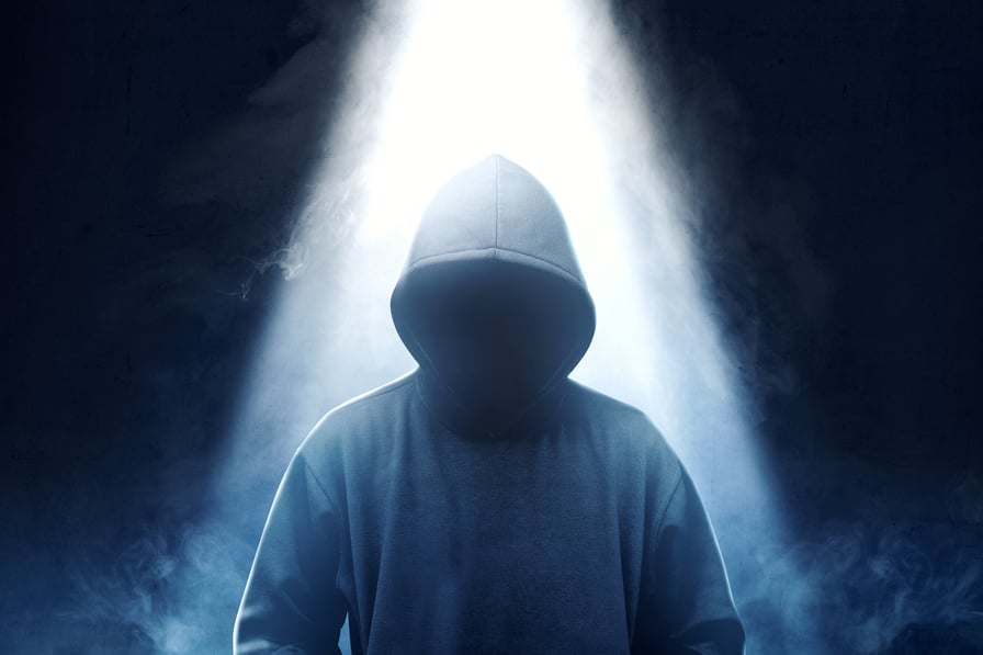 Man in dark hoodie with bright light from above.